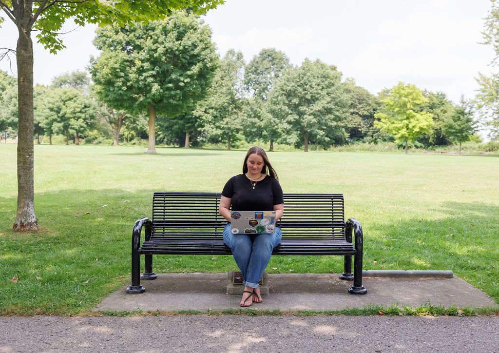 Dana, a bookkeeper, sitting on a bench writing a blog post about hst for small business.